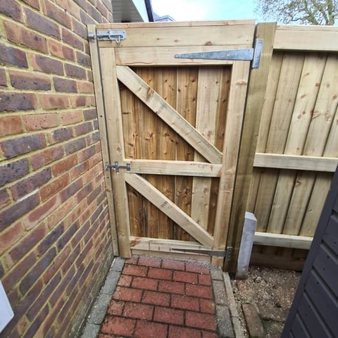 Wooden garden gate with diagonal bracing attached to a brick wall with metal hinges