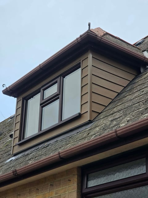 Modern dormer window with beige and brown framing on stone house roof