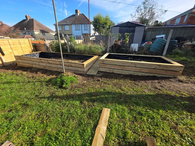 Wooden raised garden beds in a residential backyard with houses and garden structures visible in the background