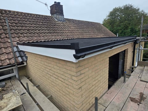 Brick utility building with black flat roof and open entrance, attached to residential house with tiled roof